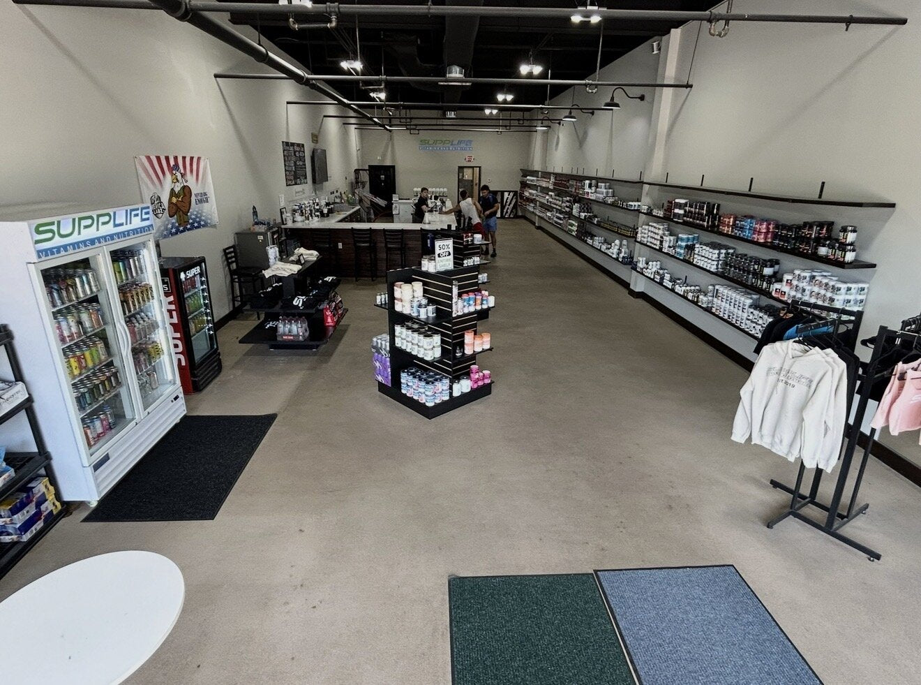 Inside a SuppLife vitamin and nutrition store — fridge, supplement wall, and shake bar
